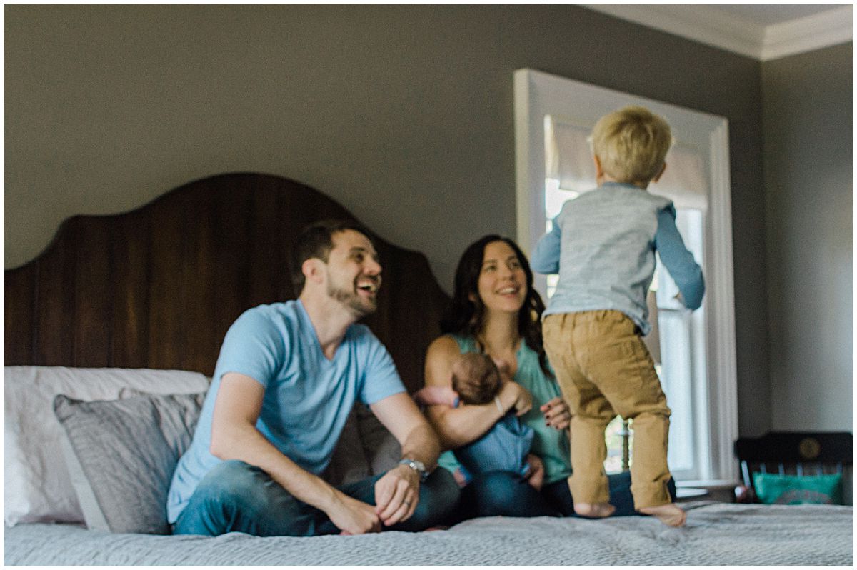little boy jumping on a big bed as his parents laugh and adore him in Essex County NJ