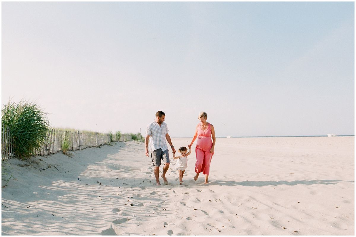 mom and dad holding hands of their little daughter during maternity photography session in Sandy Hook NJ