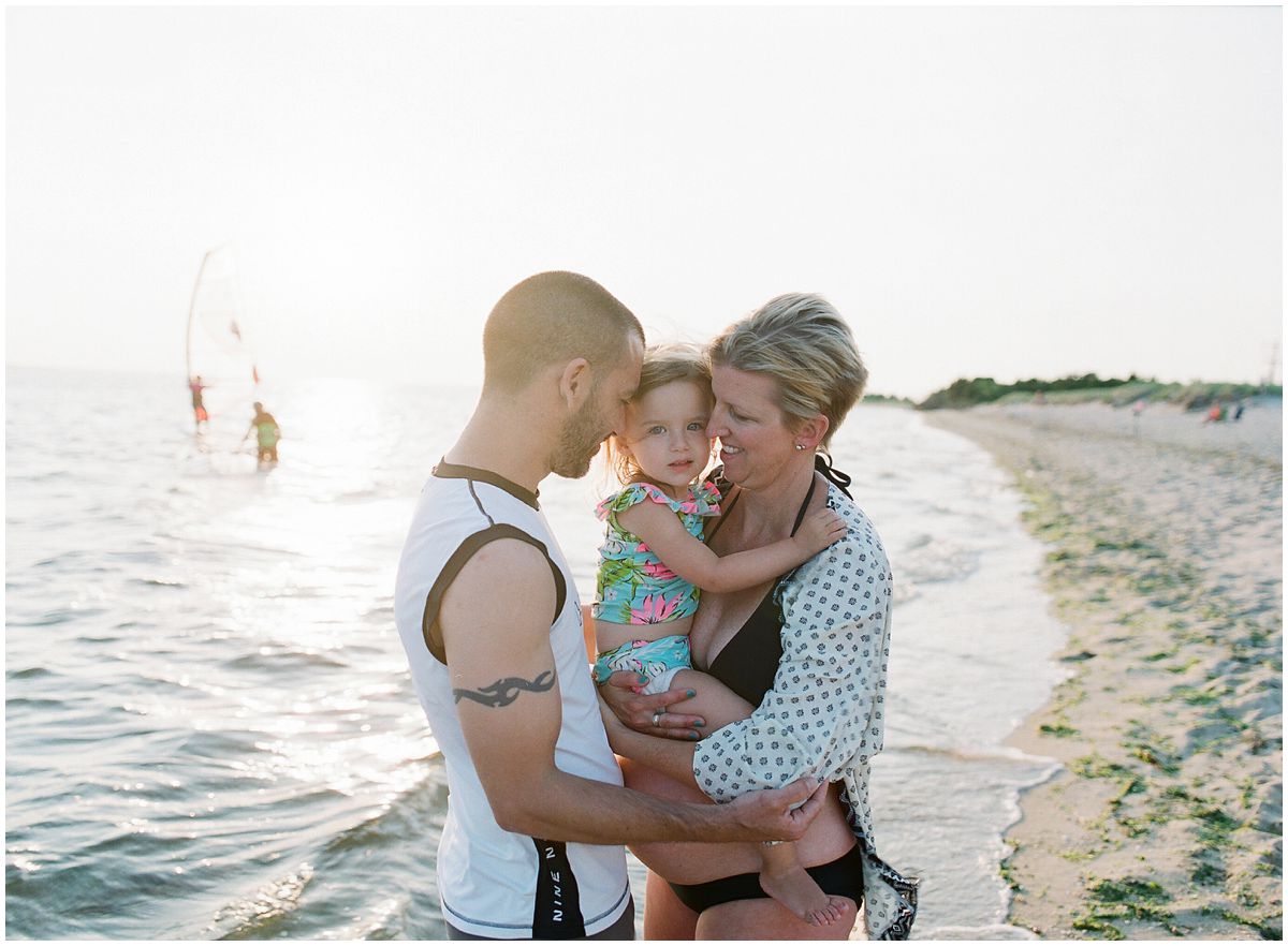 parents and little girl are hugging by the beach waves of Sandy Hook NJ
