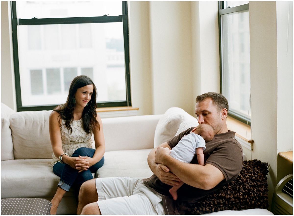 Little baby boy sleeping on his dad and mom is lovingly looking on them both in Hoboken NJ apartment