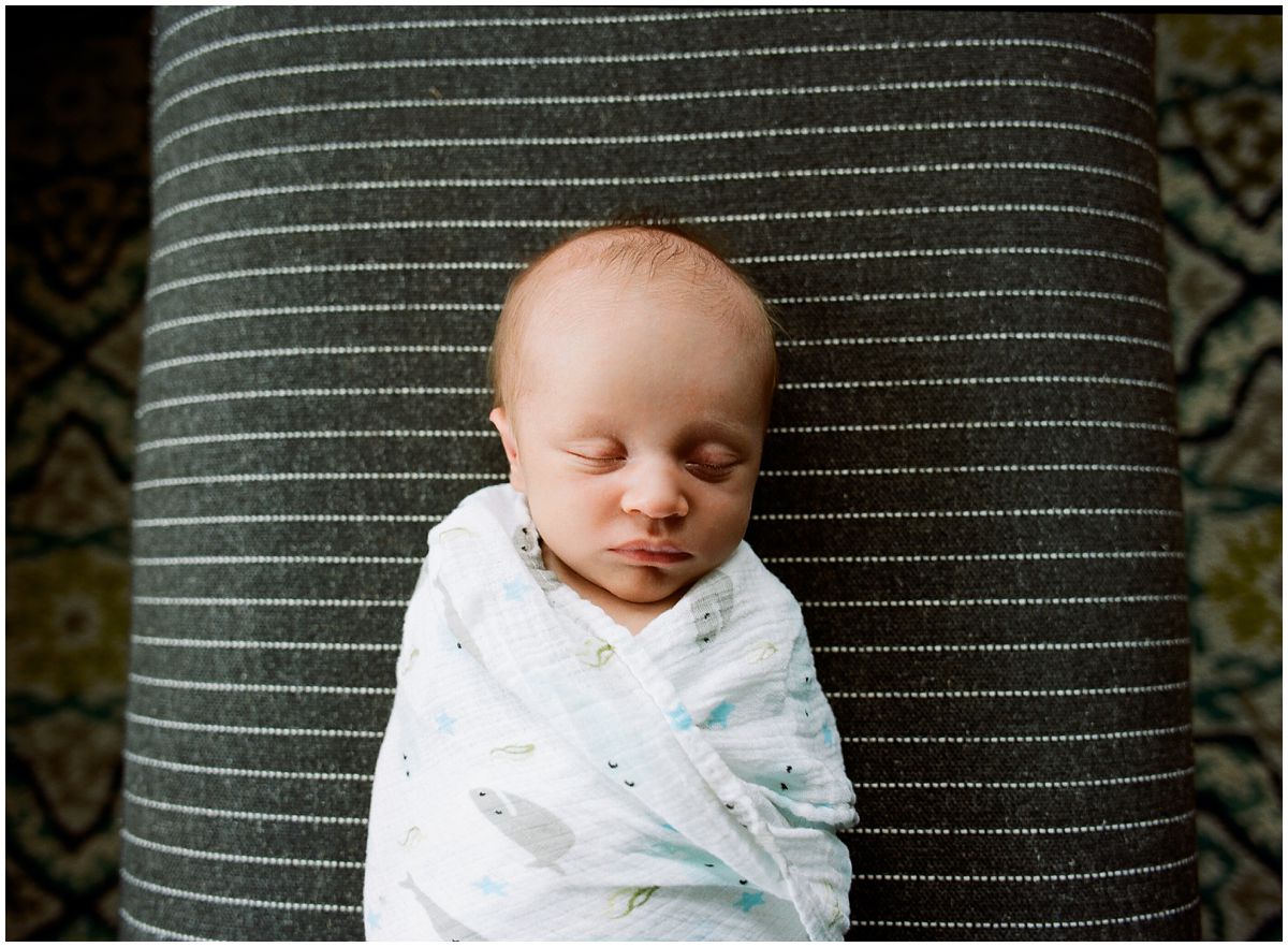 newborn baby boy swaddled and sleeping in living room on the grey ottoman in NJ home