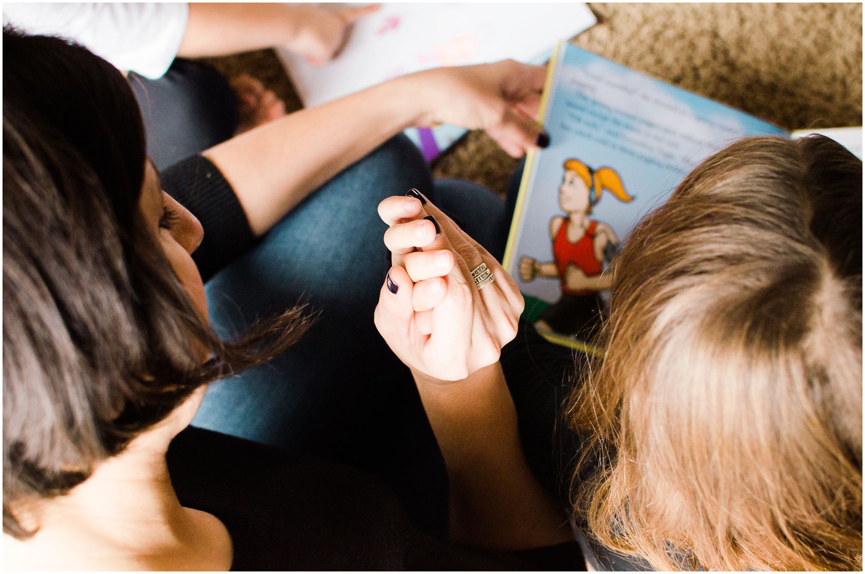 mom and daughter sitting on the floor and holding hands while reading a book together in Bergen County, NJ
