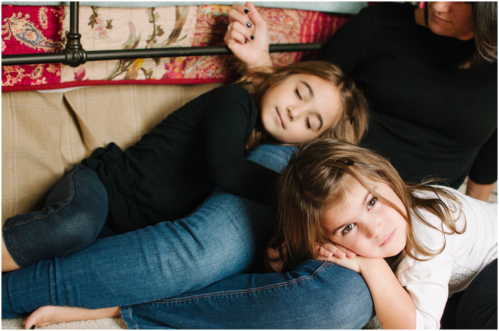 two brunette daughters with long hair are laying on mom during motherhood and family photos