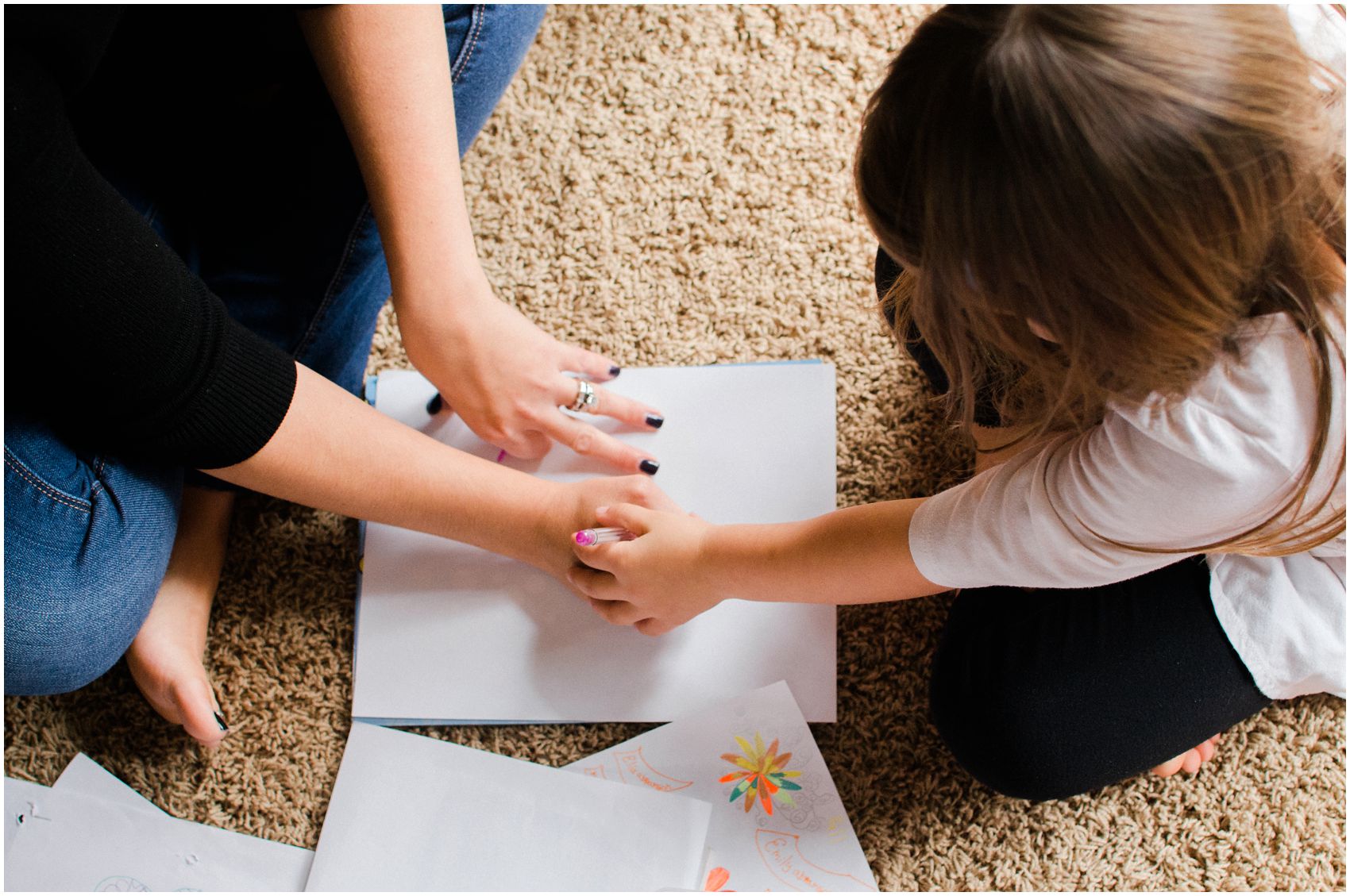 mom and daughter holding hands and coloring a paper on the floor with a pink marker