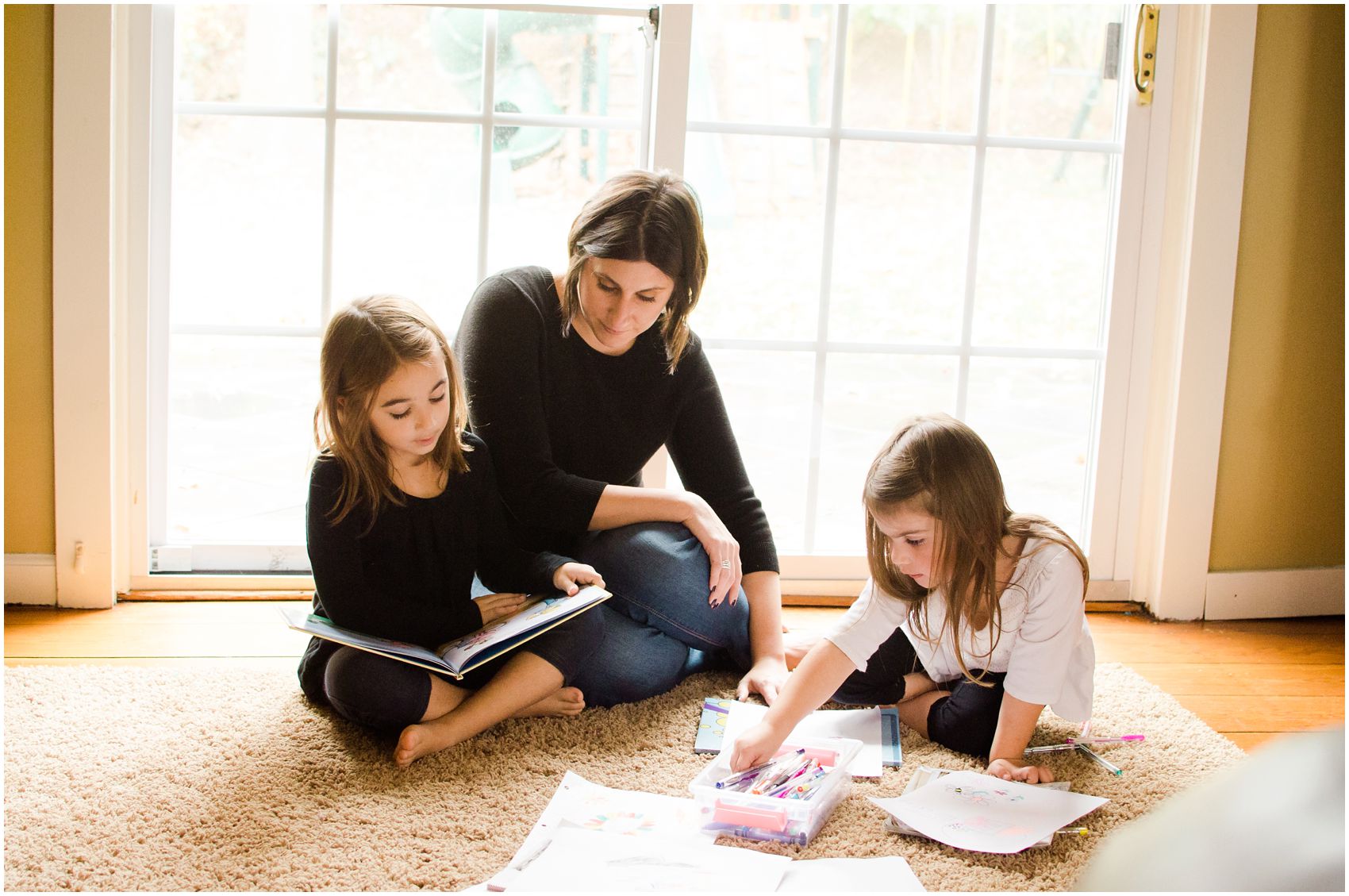 Mom is reading book with one daughter and coloring with markers with another daughter in their Maplewood, NJ home
