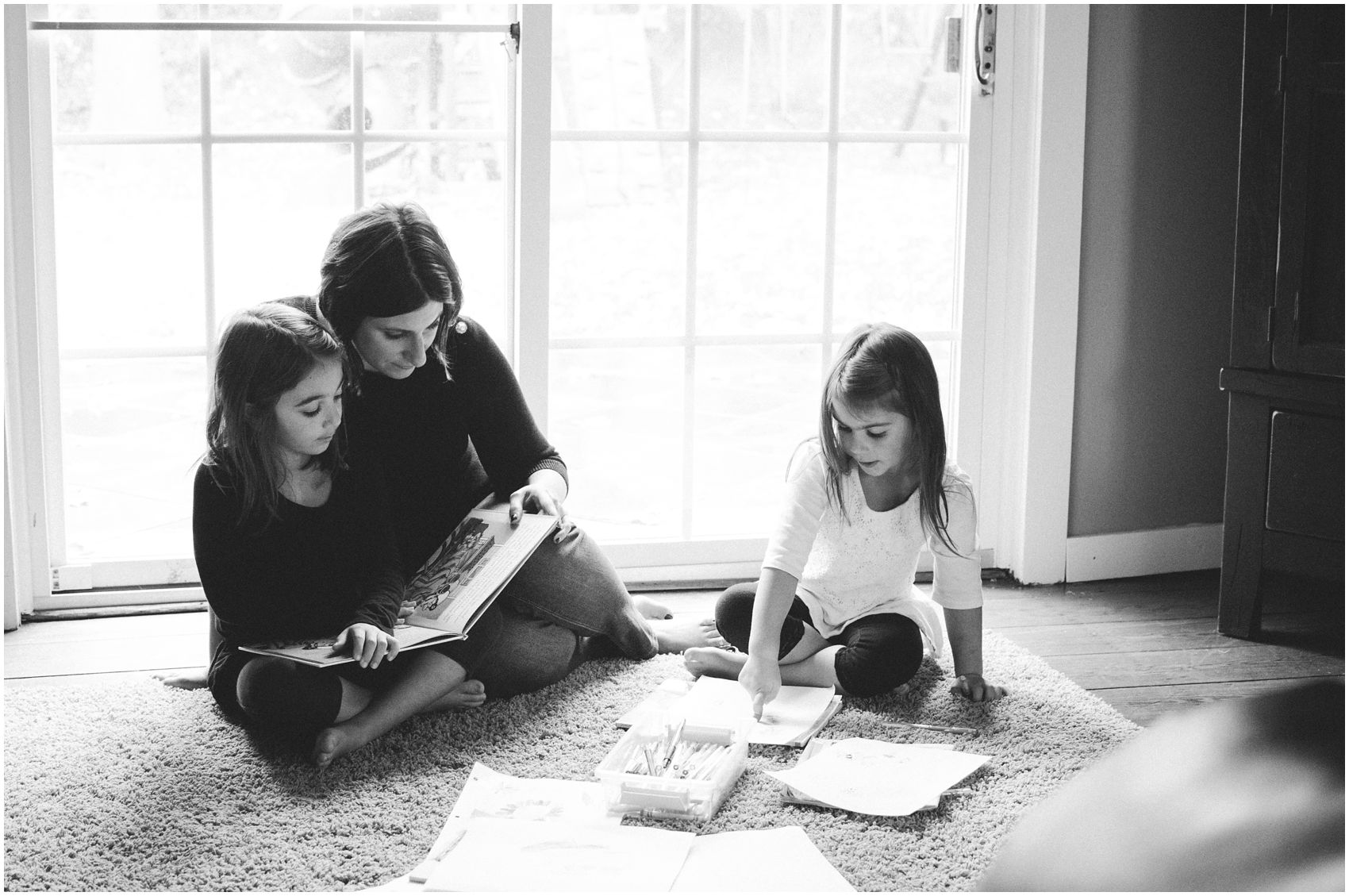 A black and white portrait of Mom reading books and coloring with her two preteen daughters in Maplewood Nj