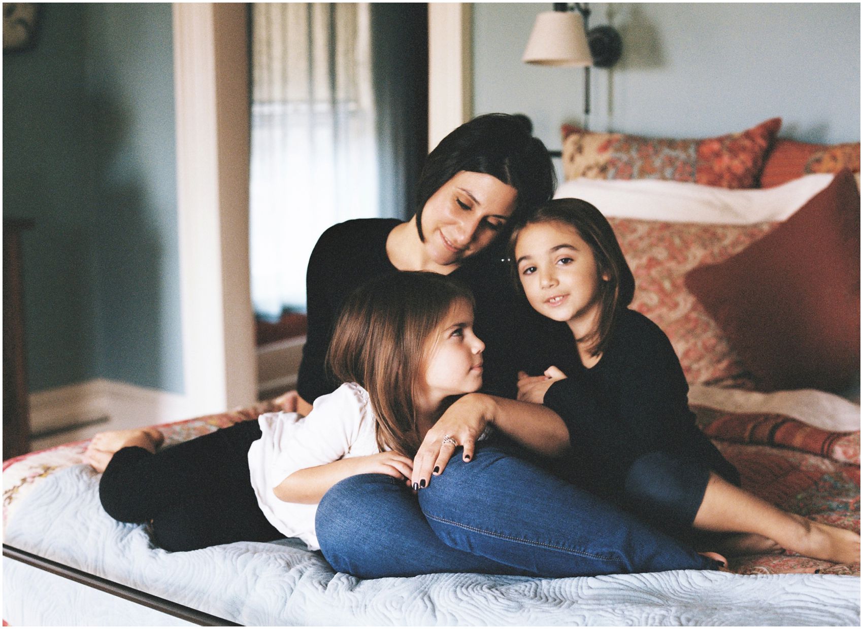 Mother and daughters snuggle together on their bed for a motherhood and family photography portrait in Tenafly, NJ