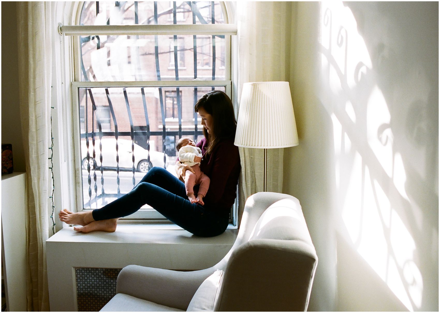 NYC Newborn Photographer Miriam Dubinsky shares tips on when is the best time to schedule the newborn photos mom holding baby girl by the window