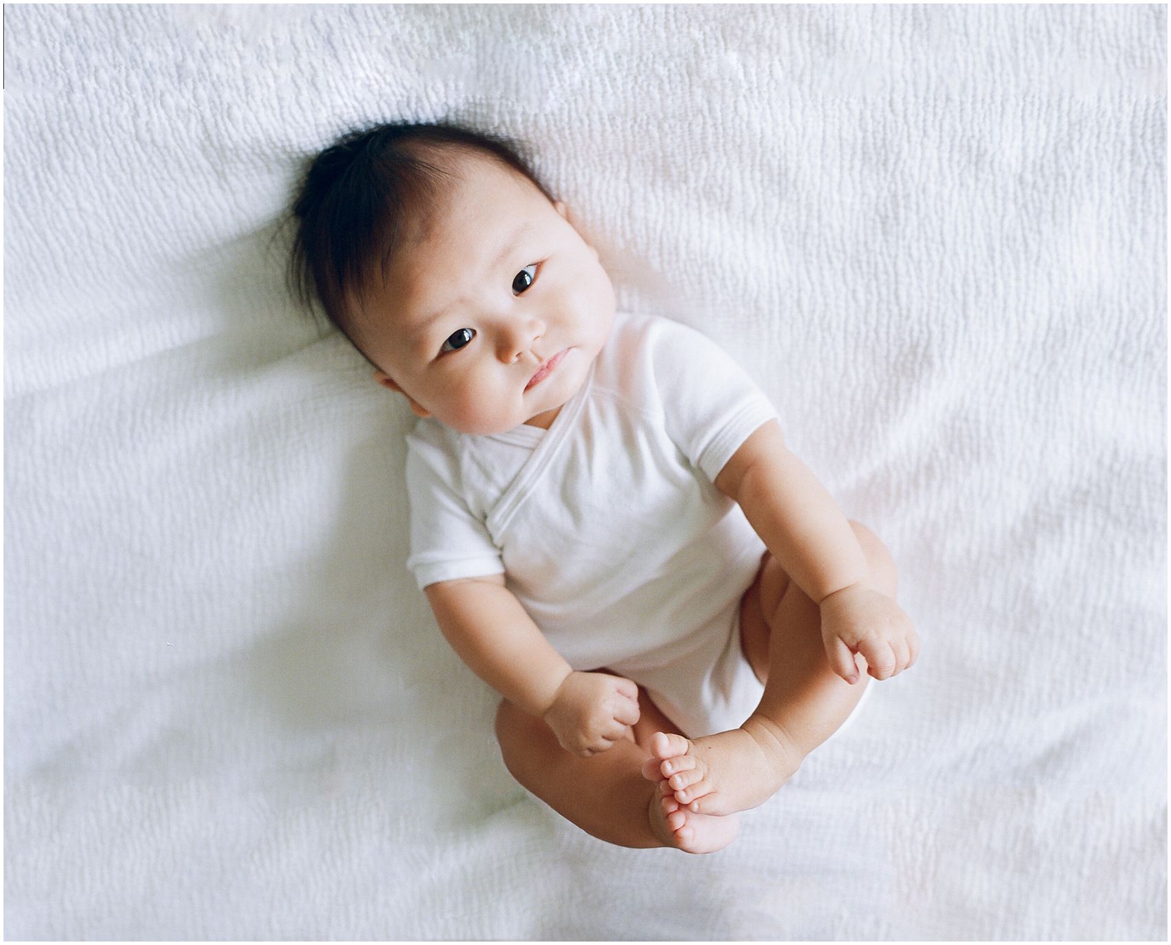 chubby 6 months old baby looking up wearing a white onesie in Jersey City, NJ home
