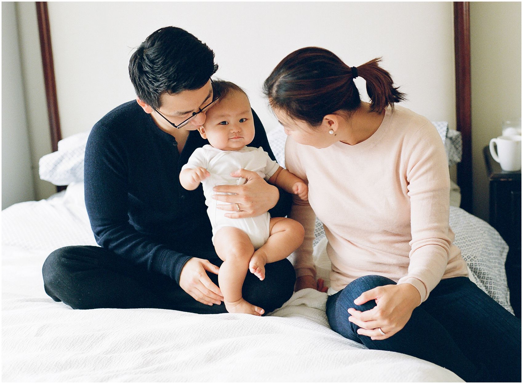 parents snuggle with their cute baby boy wearing white onesie in baby photos on bed