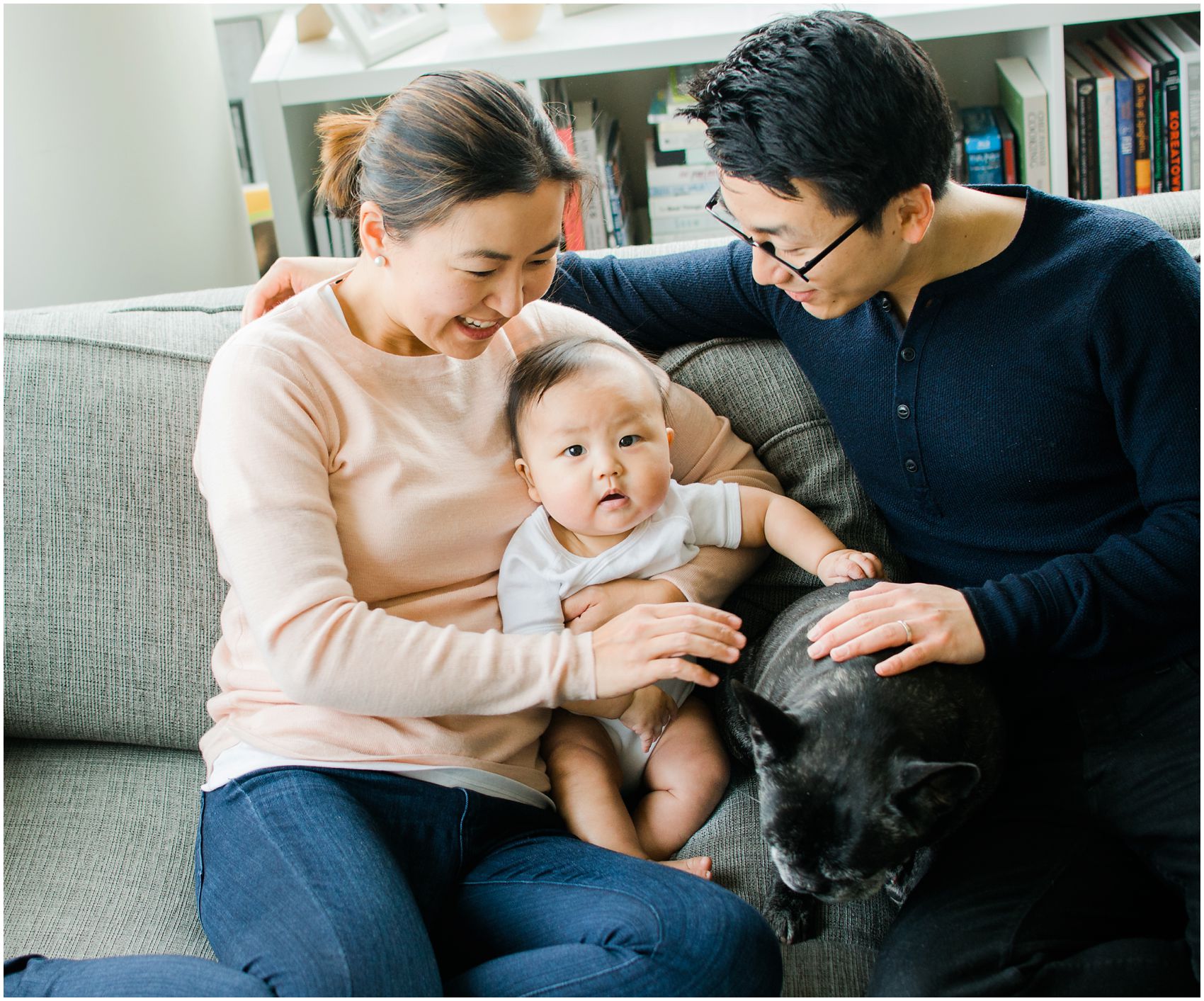 parents snuggle with baby boy and family French Bulldog on a couch in Jersey City, NJ