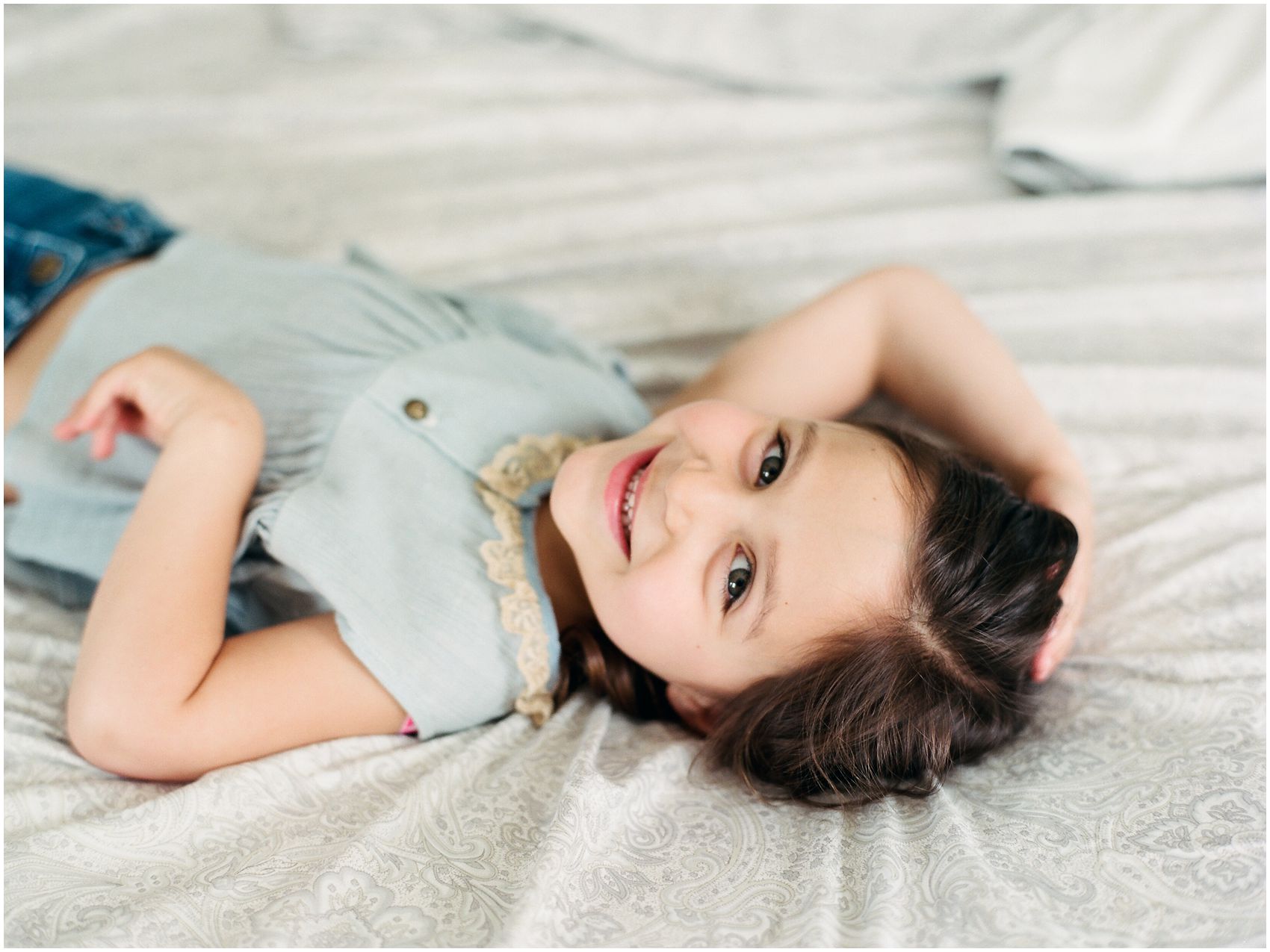little girl smiling in lifestyle family portraits in bed of her Montclair home