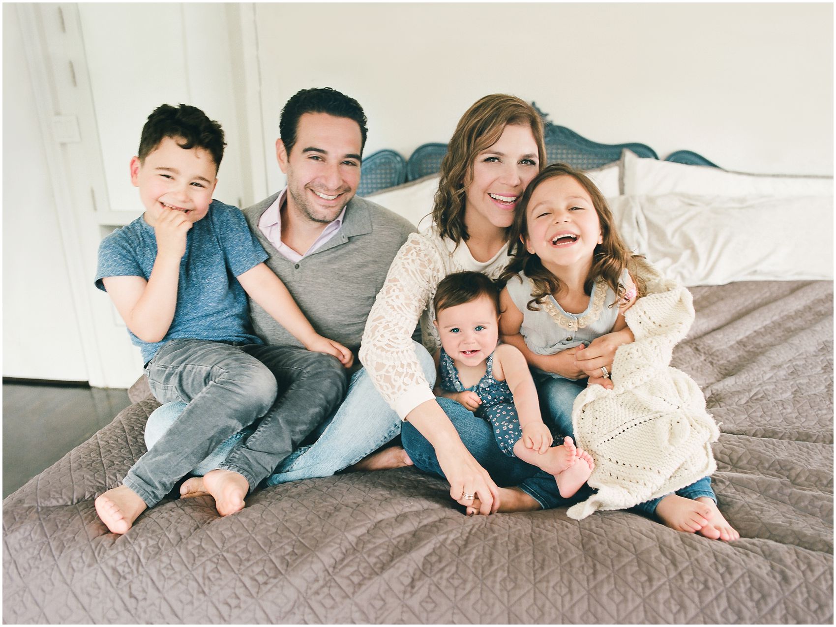 family of parents and 3 kids is all snuggled up on bed for the lifestyle family photography at home