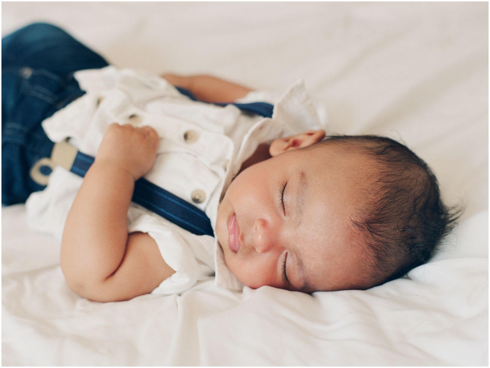 Newborn portrait of a baby boy is sleeping on white bed in NYC