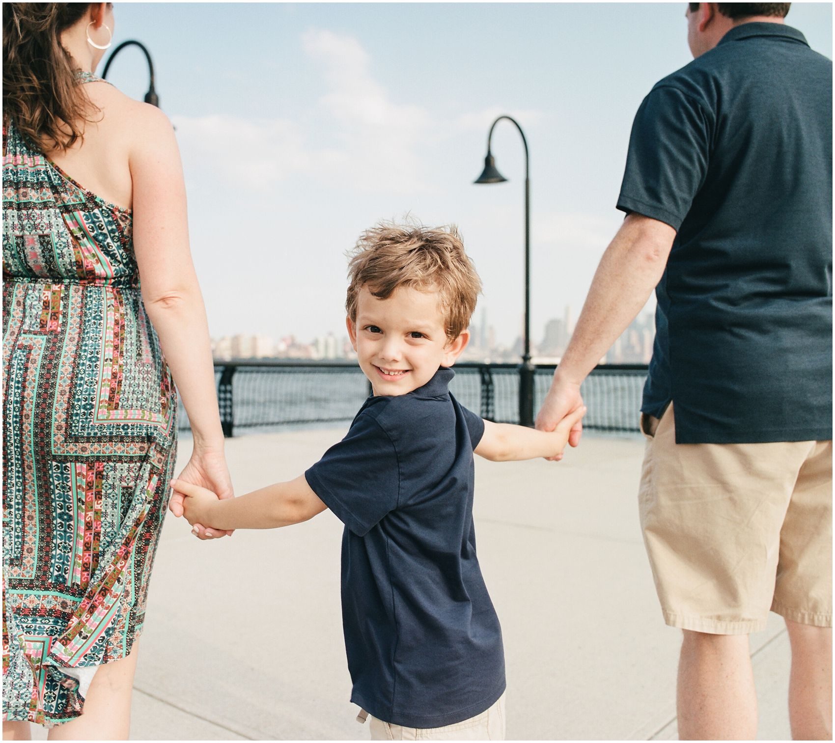 Summer family lifestyle photos of a boy holding his parents' hands by NYC