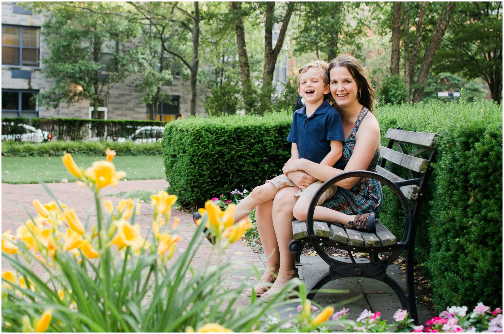 Family fun in the summer with mom and sun sitting and laughing on a bench in the Hoboken park