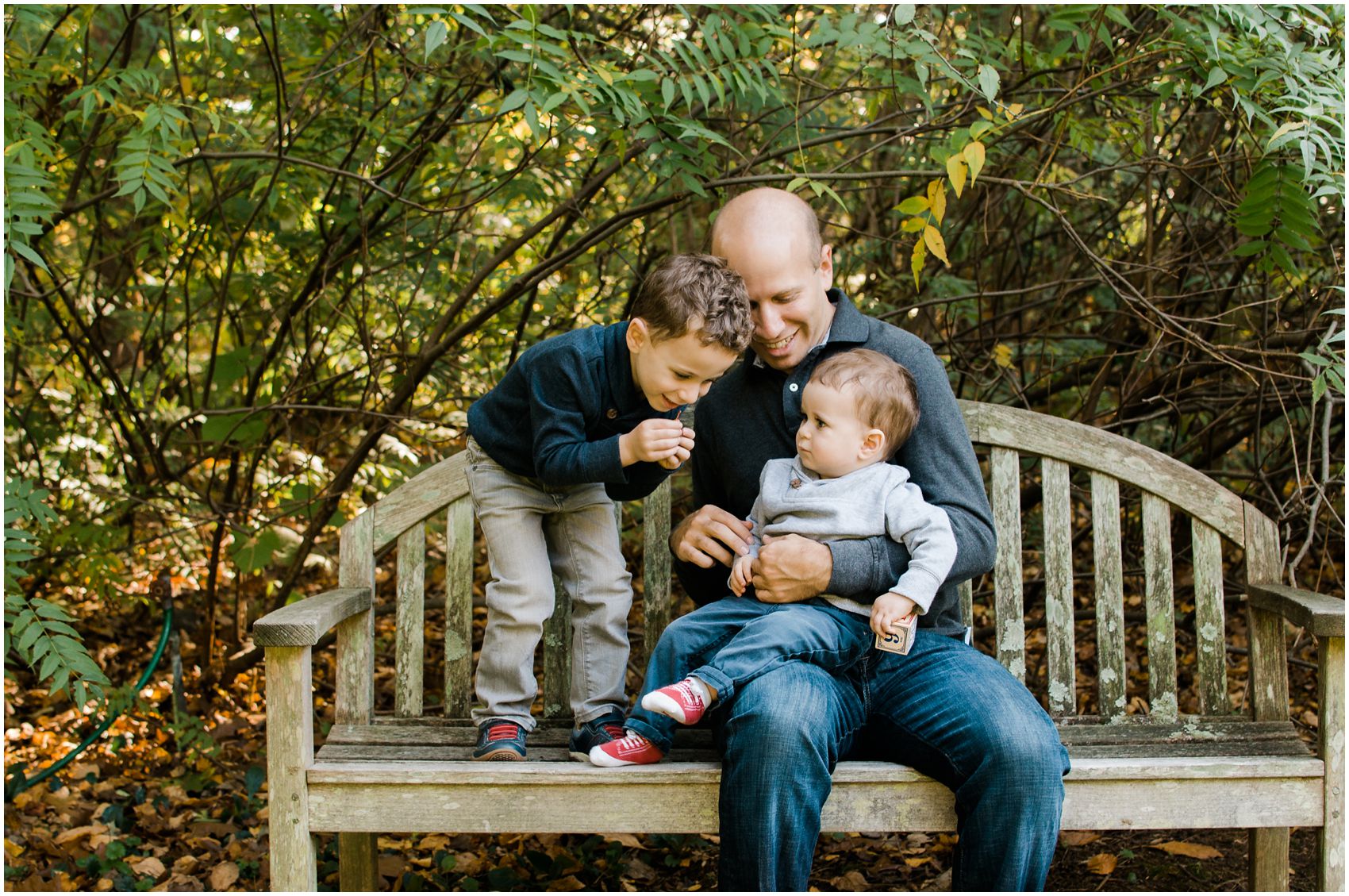 Father is sitting on a bench with his two boys wearing gray and navy clothing