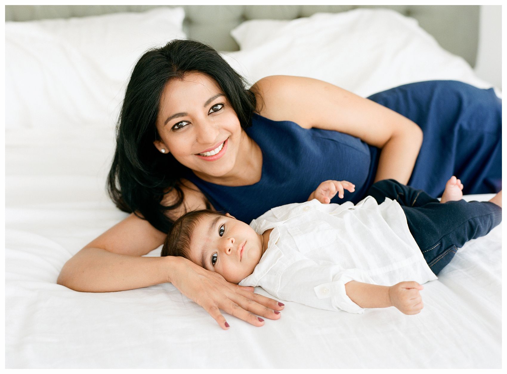 gorgeous mom in blue dress and one month baby boy laying in bed for a mini photo session