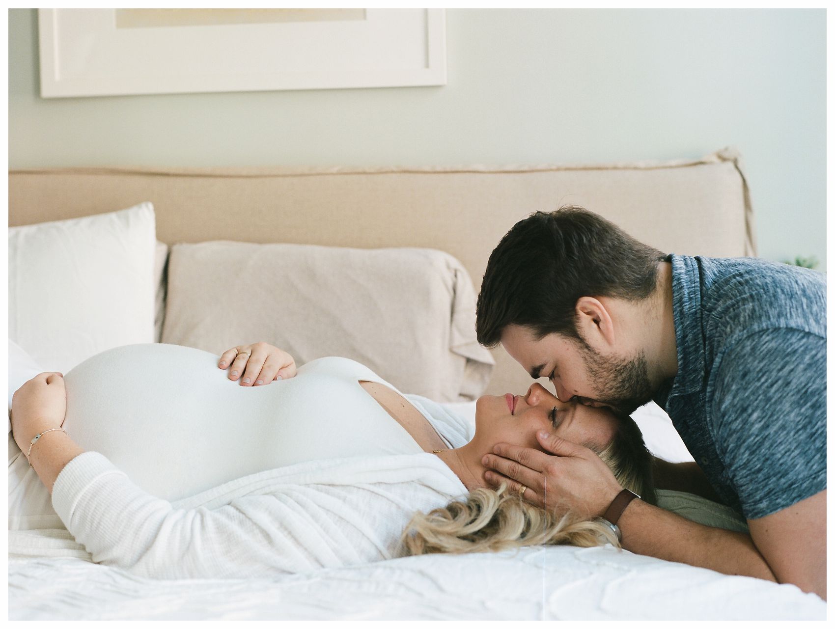 NYC best voted maternity photographer Miriam Dubinsky photographs a couple in their home when the husband is kissing passionately his pregnant wife on her forehead