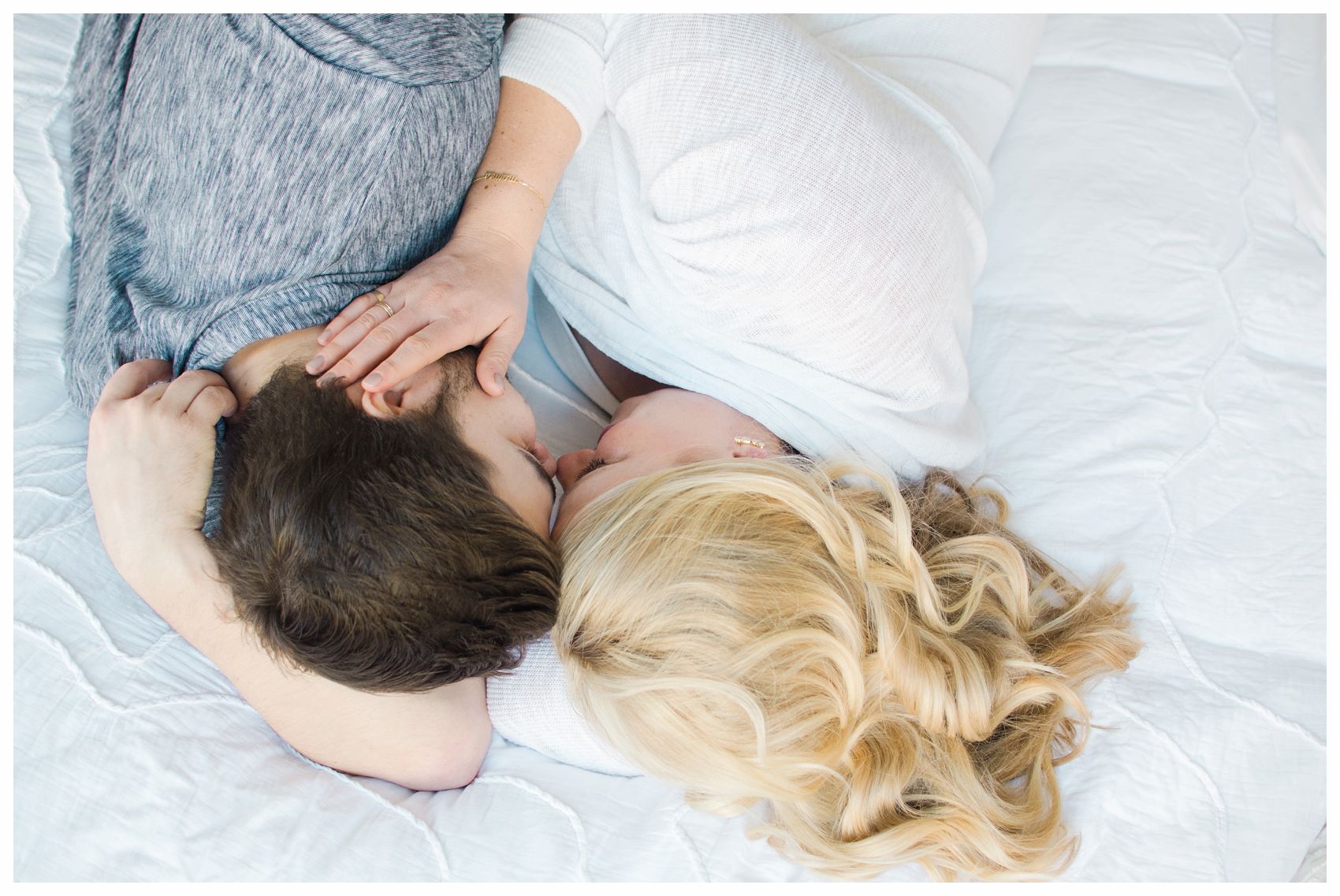mom and dad snuggling on white comforter in bed during their in-home maternity session