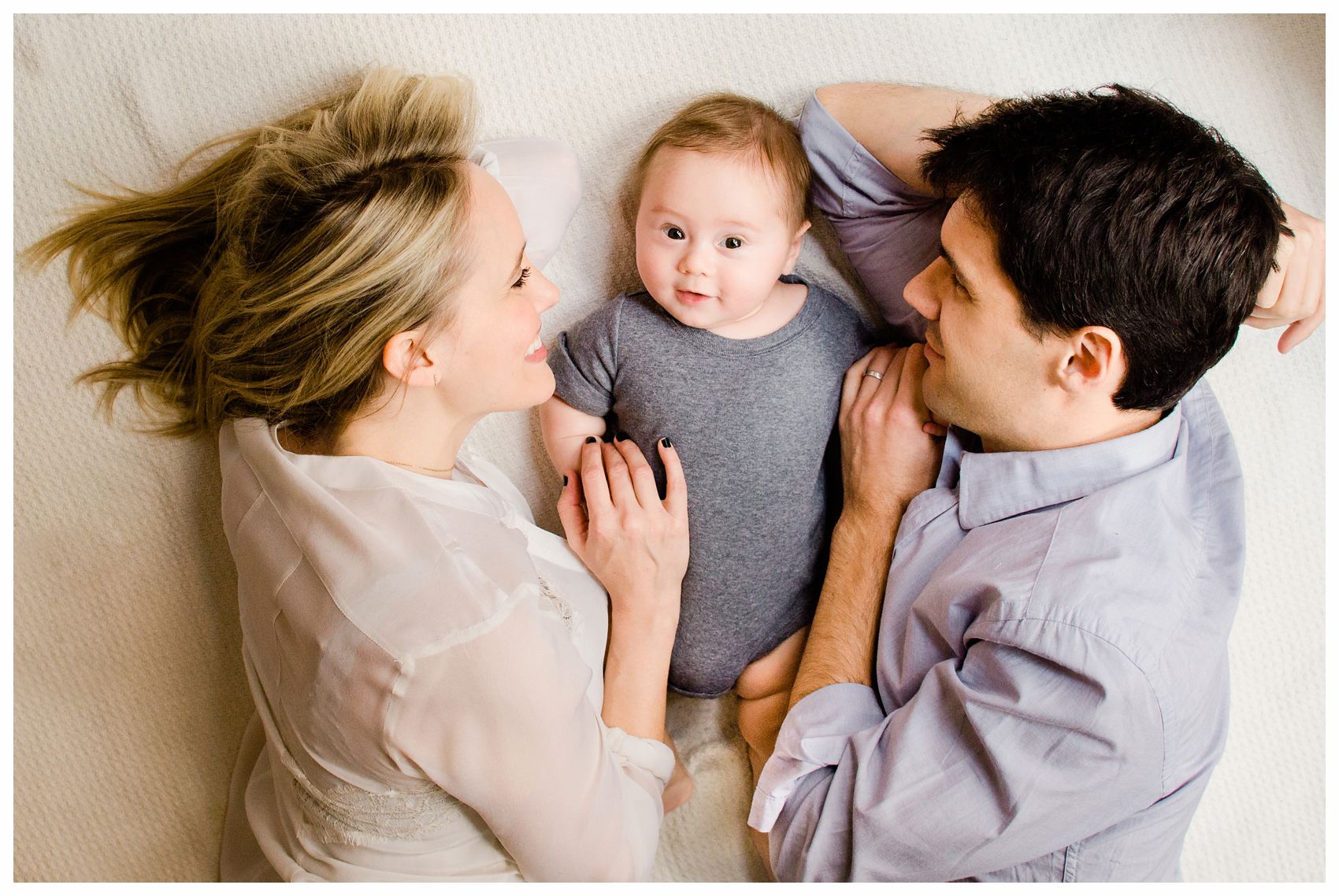 mom and dad snuggling with their adorable chubby baby boy in onesie on white blanket in Hoboken NJ