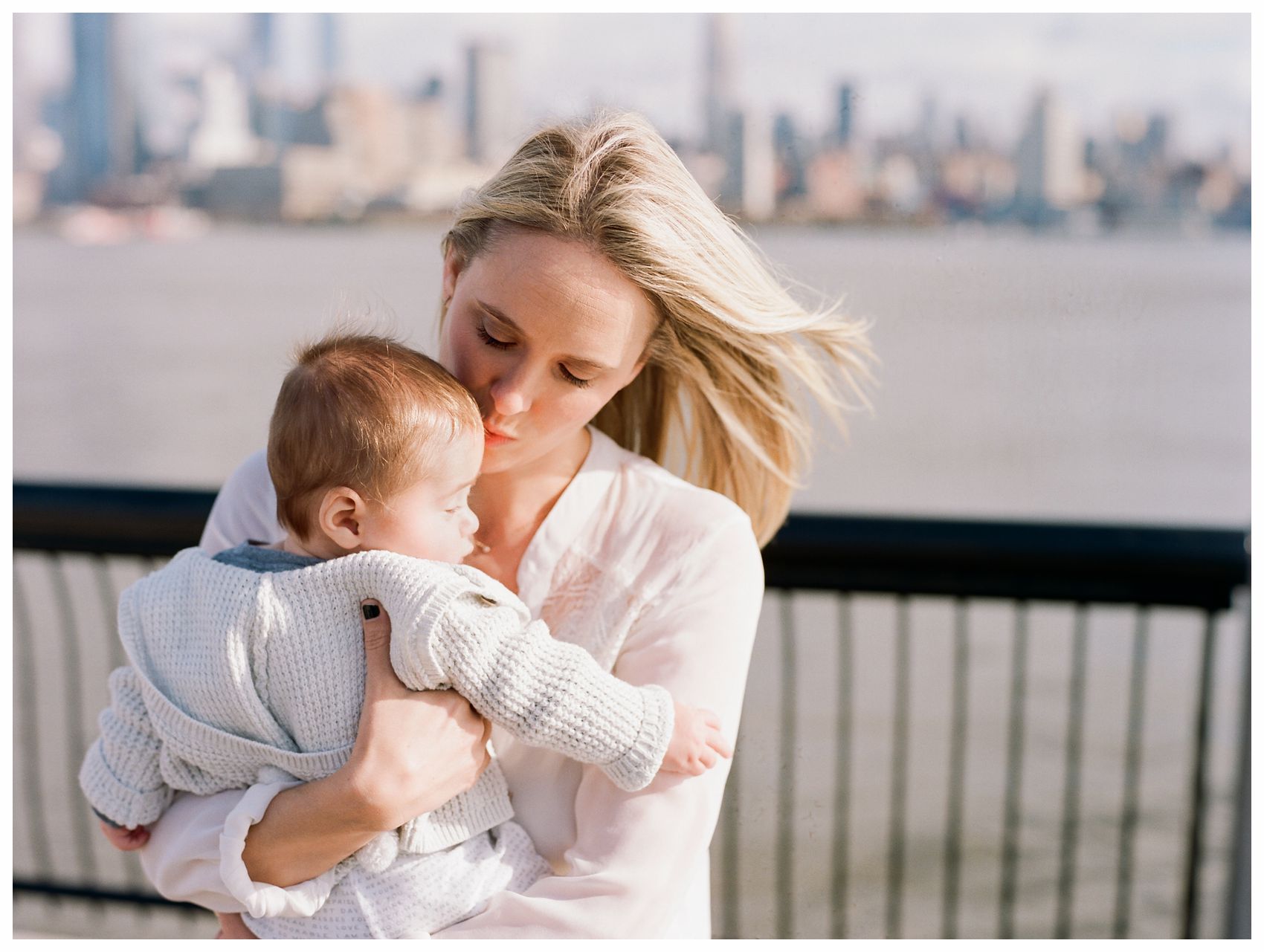 mom kissing her baby boy by Hoboken waterfront behind NYC Skyline