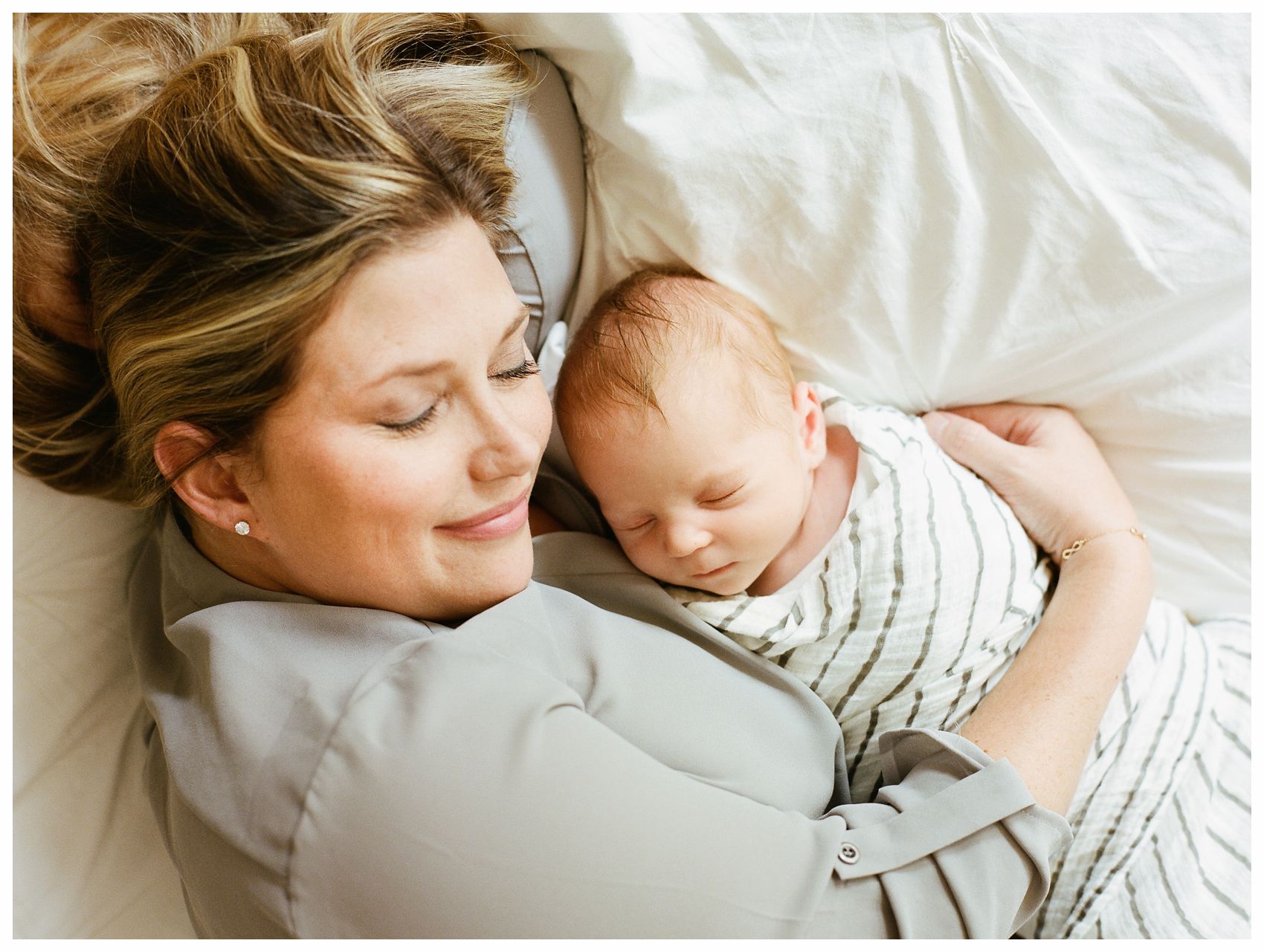 happy mom laying in bed with her baby boy swaddled next to her