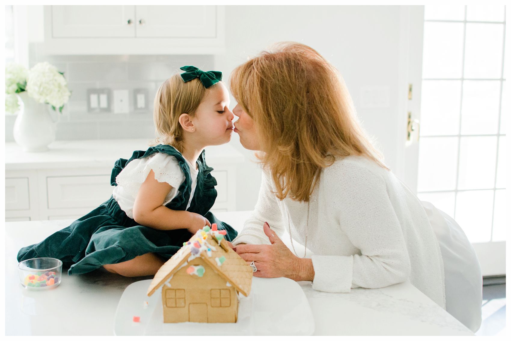 little girl kissing her grandmother in the kitchen next to gingerbread house in Essex County NJ